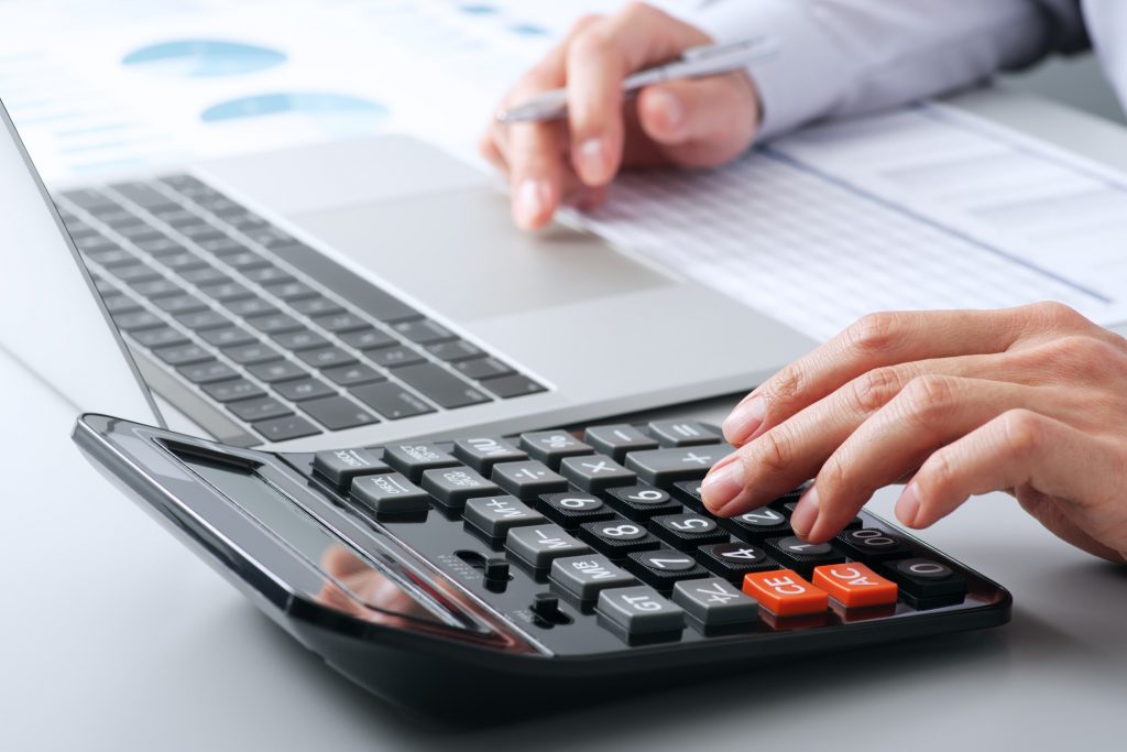 デスクで電卓に入力しながらパソコン作業をする手元