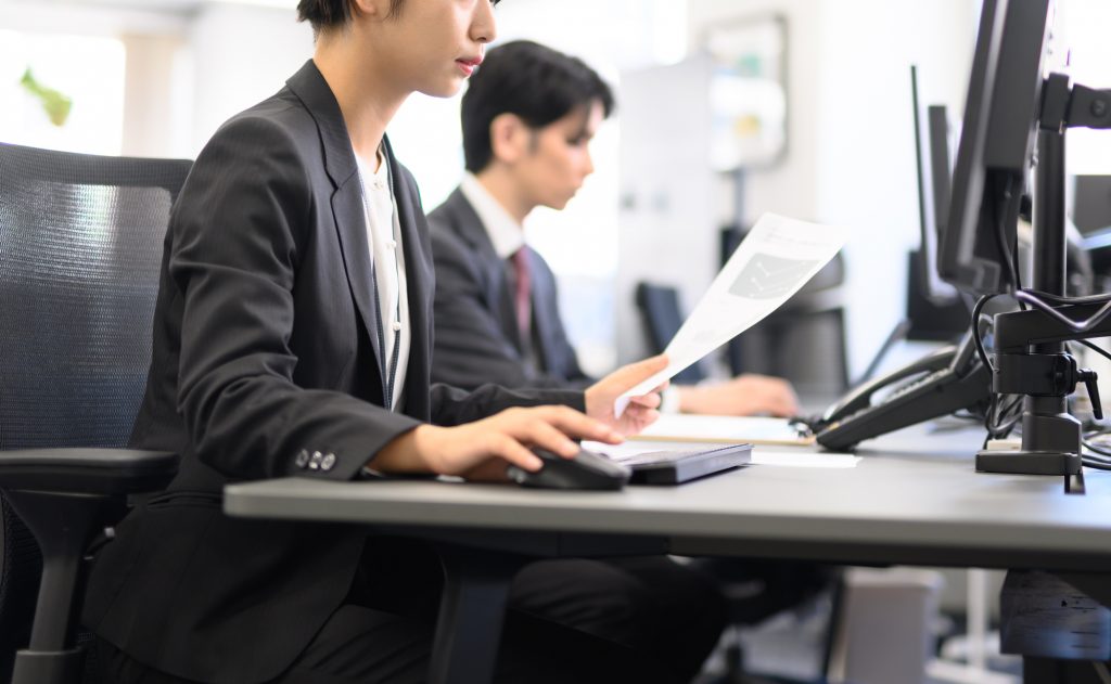 資料を手にパソコン作業をする人のビジネスパーソン
