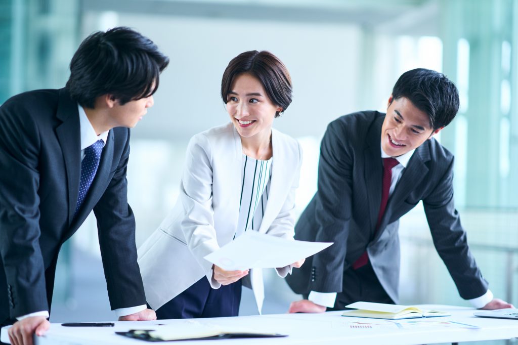 資料を手にして笑顔で会話をする3人のビジネスパーソン
