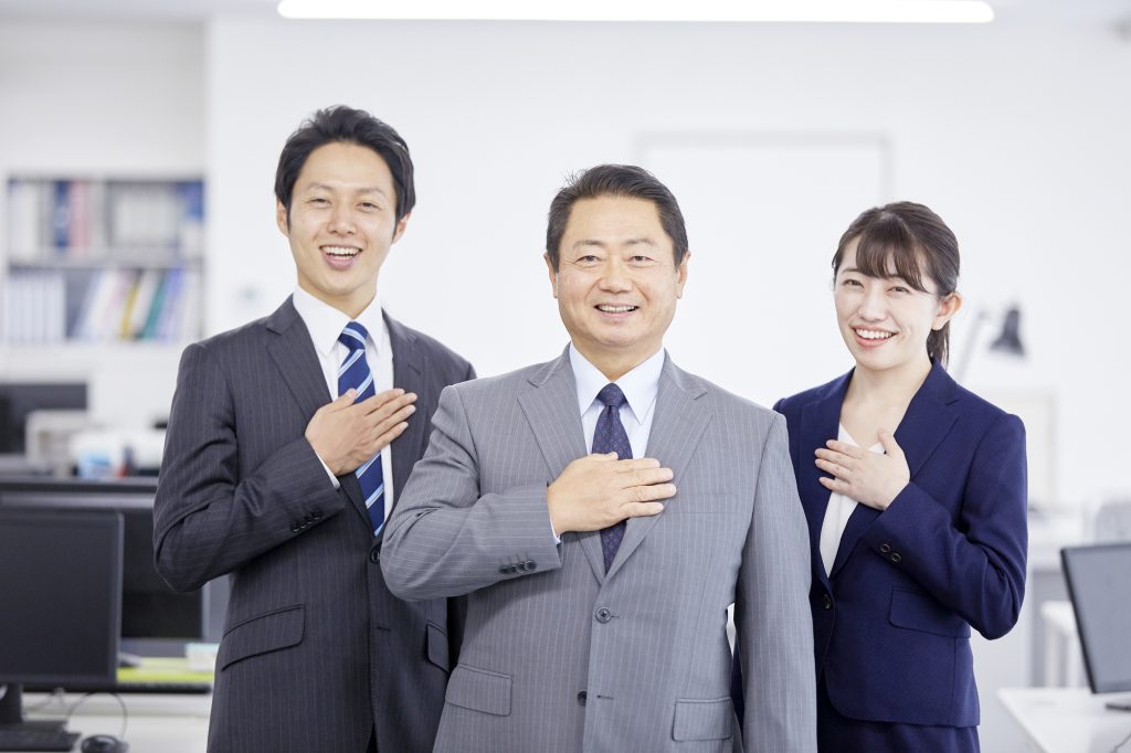 胸に手を当てて笑顔を浮かべる3人のビジネスパーソン
