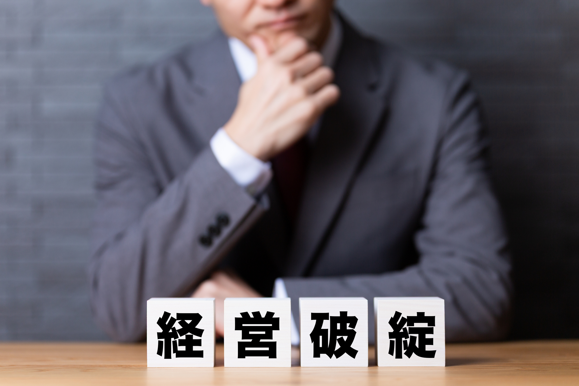 経営破綻と書かれたブロックの前で悩むビジネスパーソン