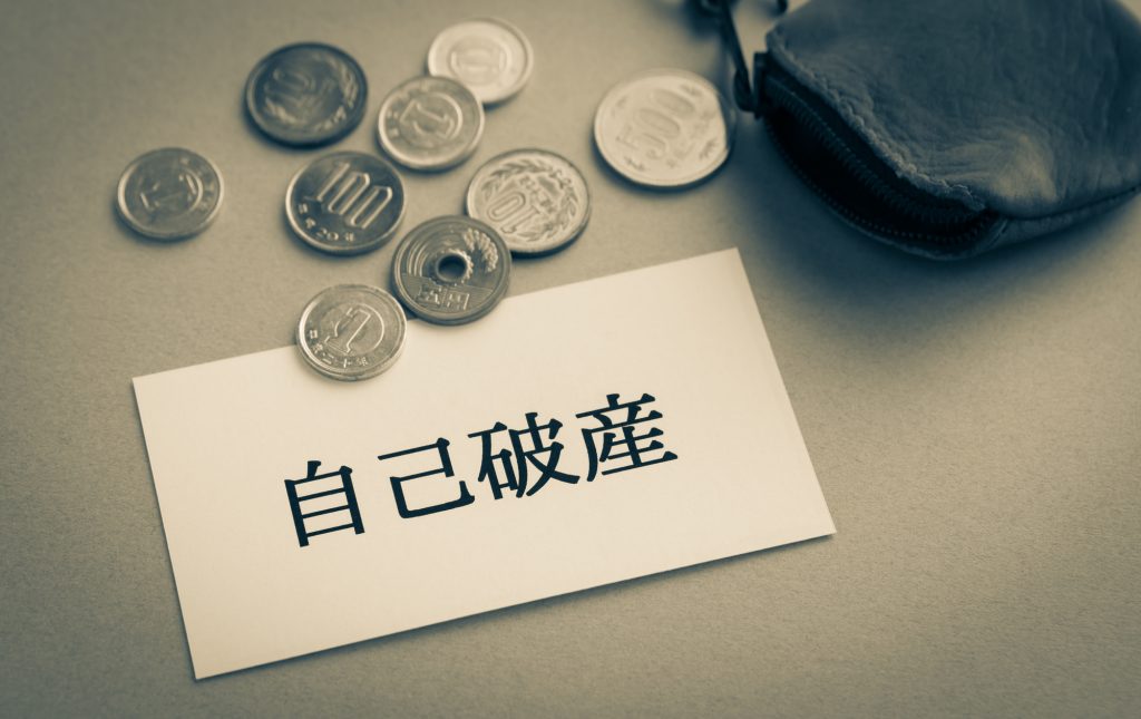 自己破産と書かれた紙と小銭とコインケースが置かれた様子