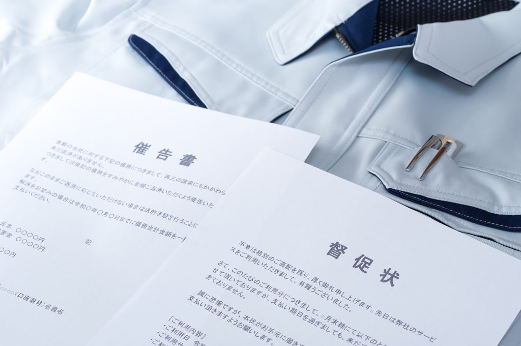作業着の上に置かれた督促状と催告書