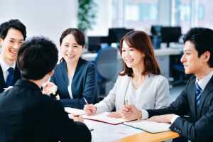 デスクに資料を置いて打ち合わせする5人のビジネスパーソン