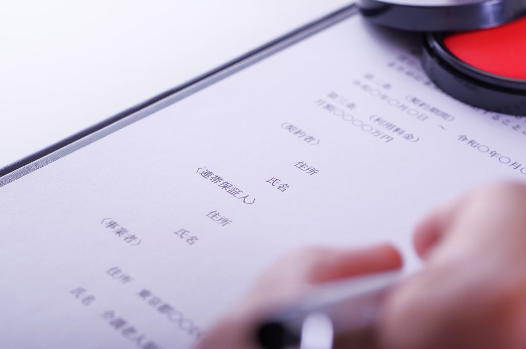 連帯保証人などが書かれた書類にサインする手元
