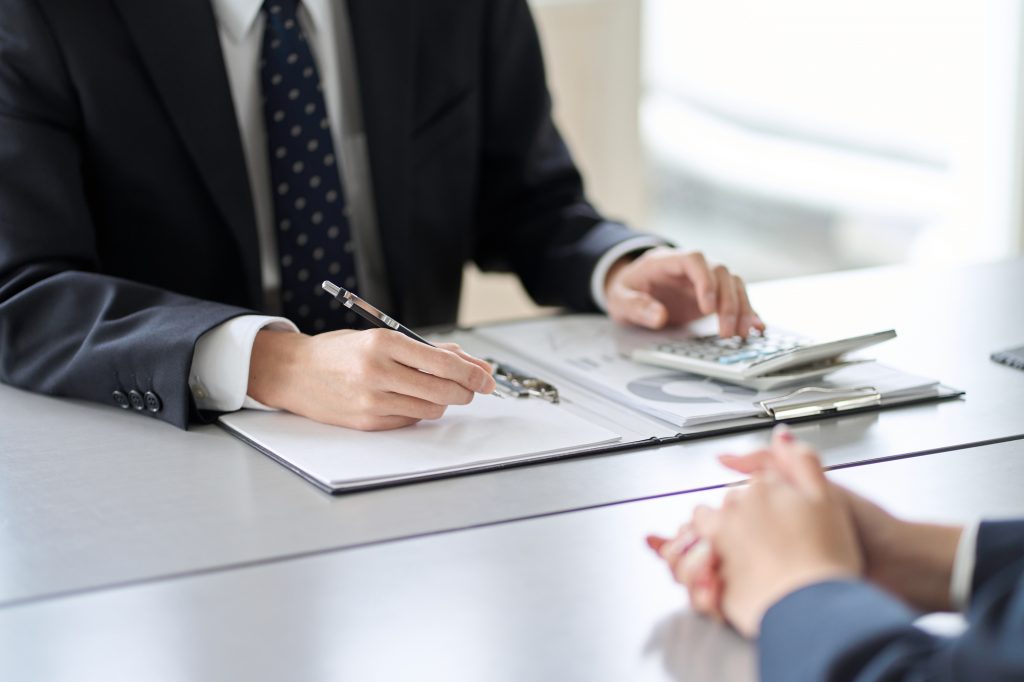 デスクの上で資料と電卓を置いて商談する2人のビジネスパーソン