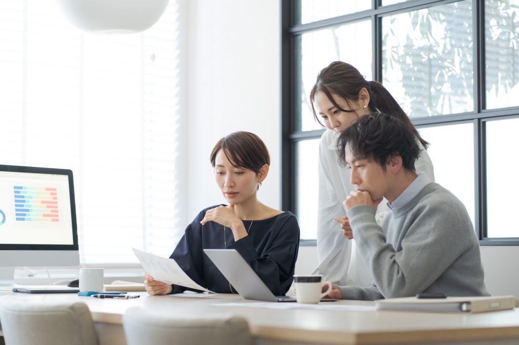 資料とパソコンを前にしてミーティングする3人のビジネスパーソン