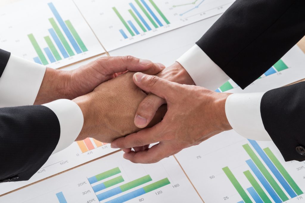 データが描かれた資料の上で握手を交わす2人のビジネスパーソン