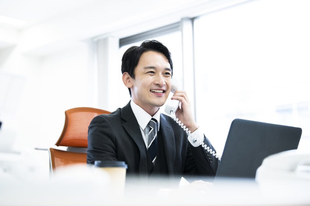 デスクで電話をしながらほほ笑むビジネスパーソン
