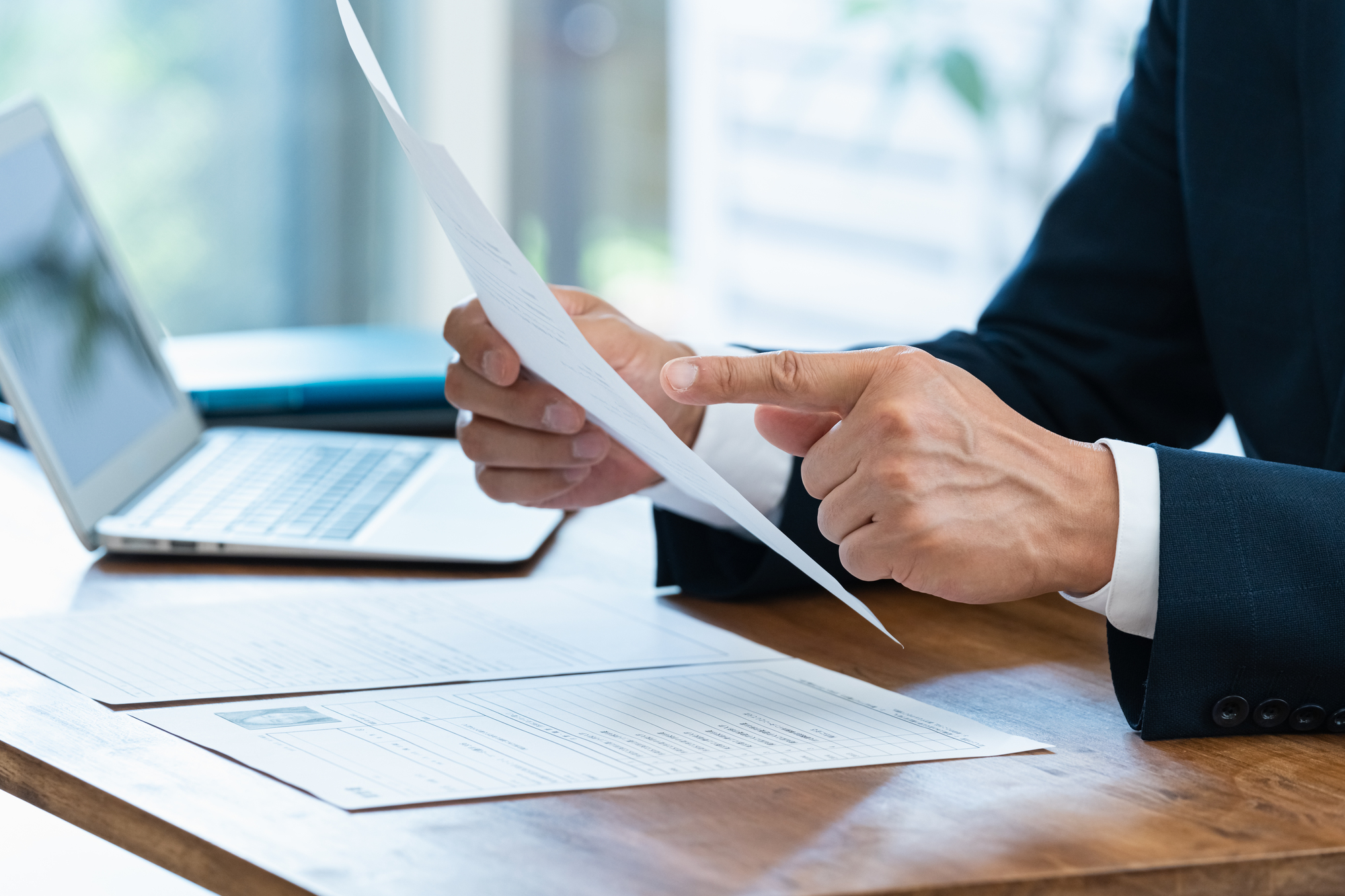 パソコンが置かれたデスクの上で資料を確認するビジネスパーソンの手元
