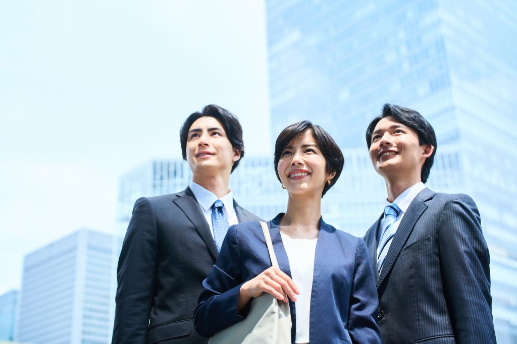 オフィスの前で笑顔で遠くを見つめる3人のビジネスパーソン