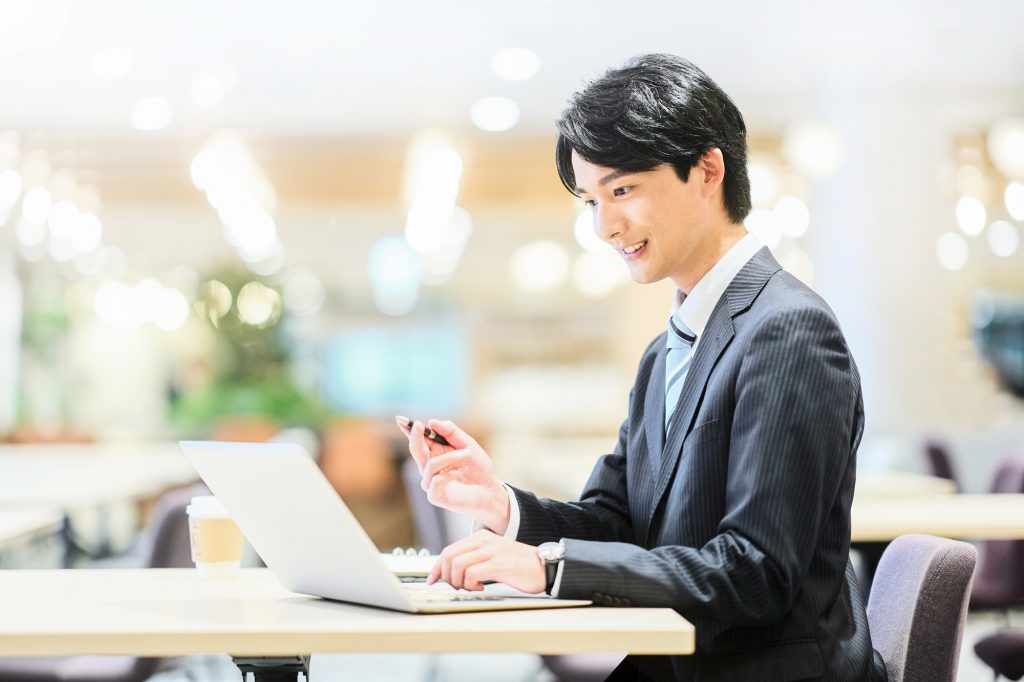 パソコンの前でボールペンを持ちながらほほ笑むビジネスパーソン