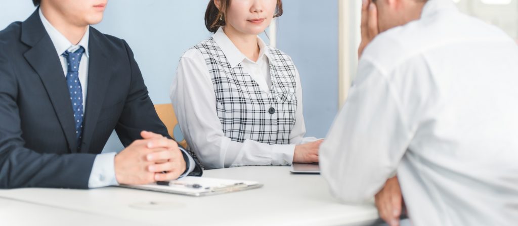 頭を悩ませるビジネスパーソンの話を聞く2人のビジネスパーソン