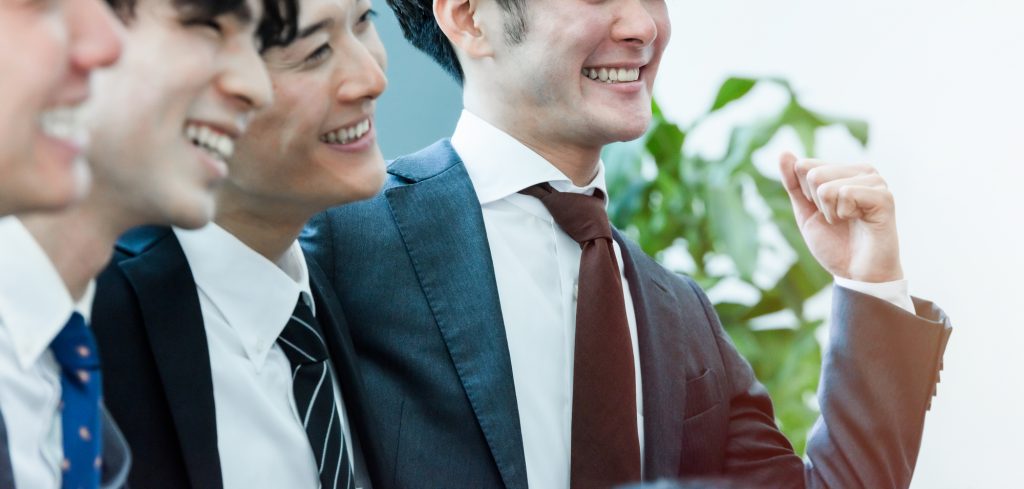 笑顔でガッツポーズをするビジネスパーソンと肩を組む3人のビジネスパーソン
