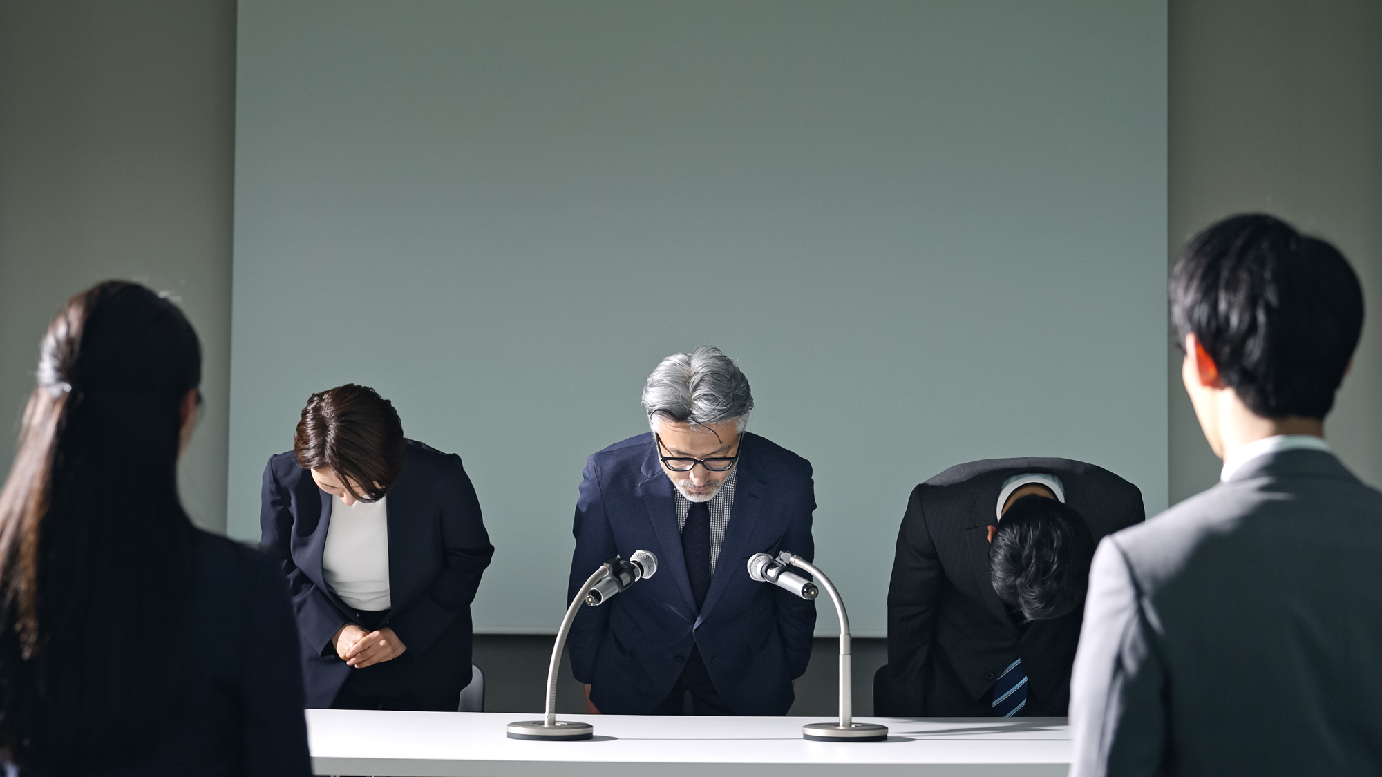 会見で頭を下げる3人のビジネスパーソン