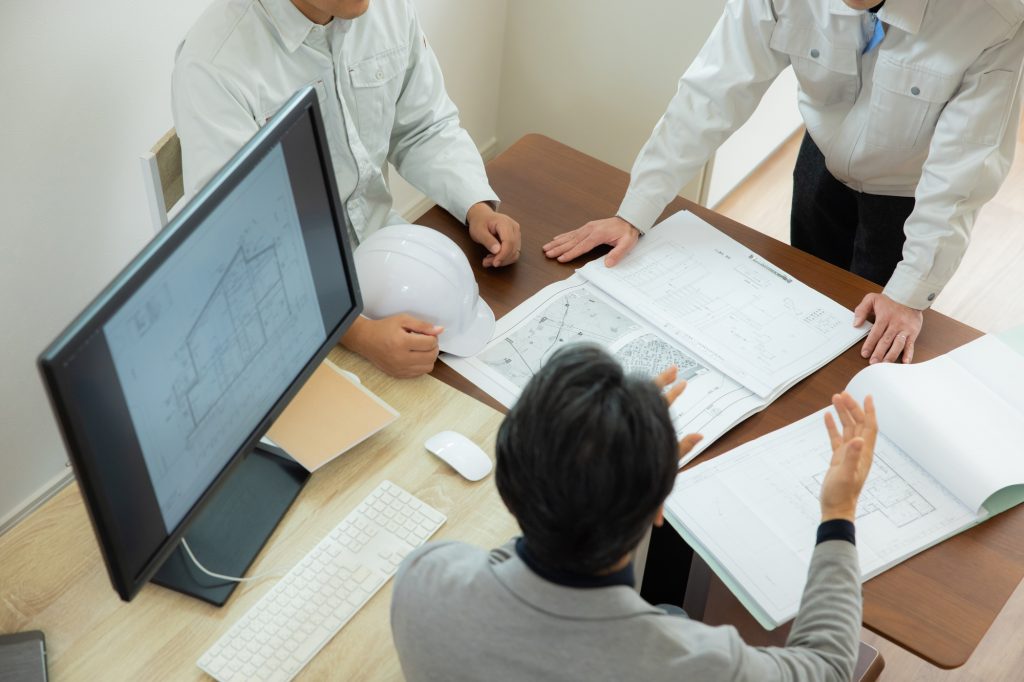 デスクにパソコンと資料を置いて打ち合わせする3人のビジネスパーソン