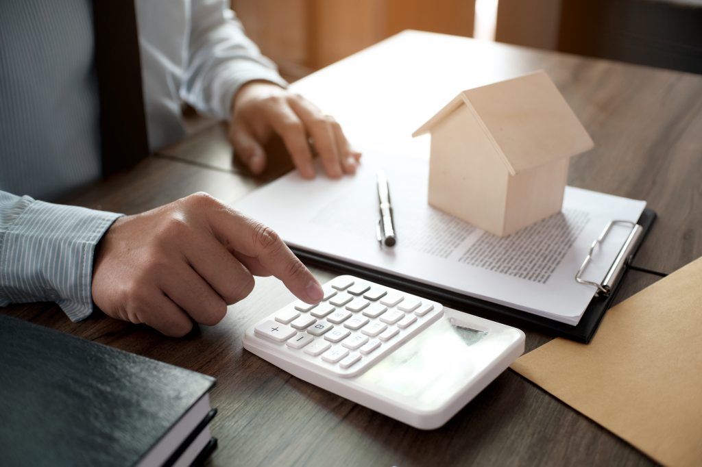 デスクの上に書類と家の形をしたブロックと電卓を置いて作業する男性の手元