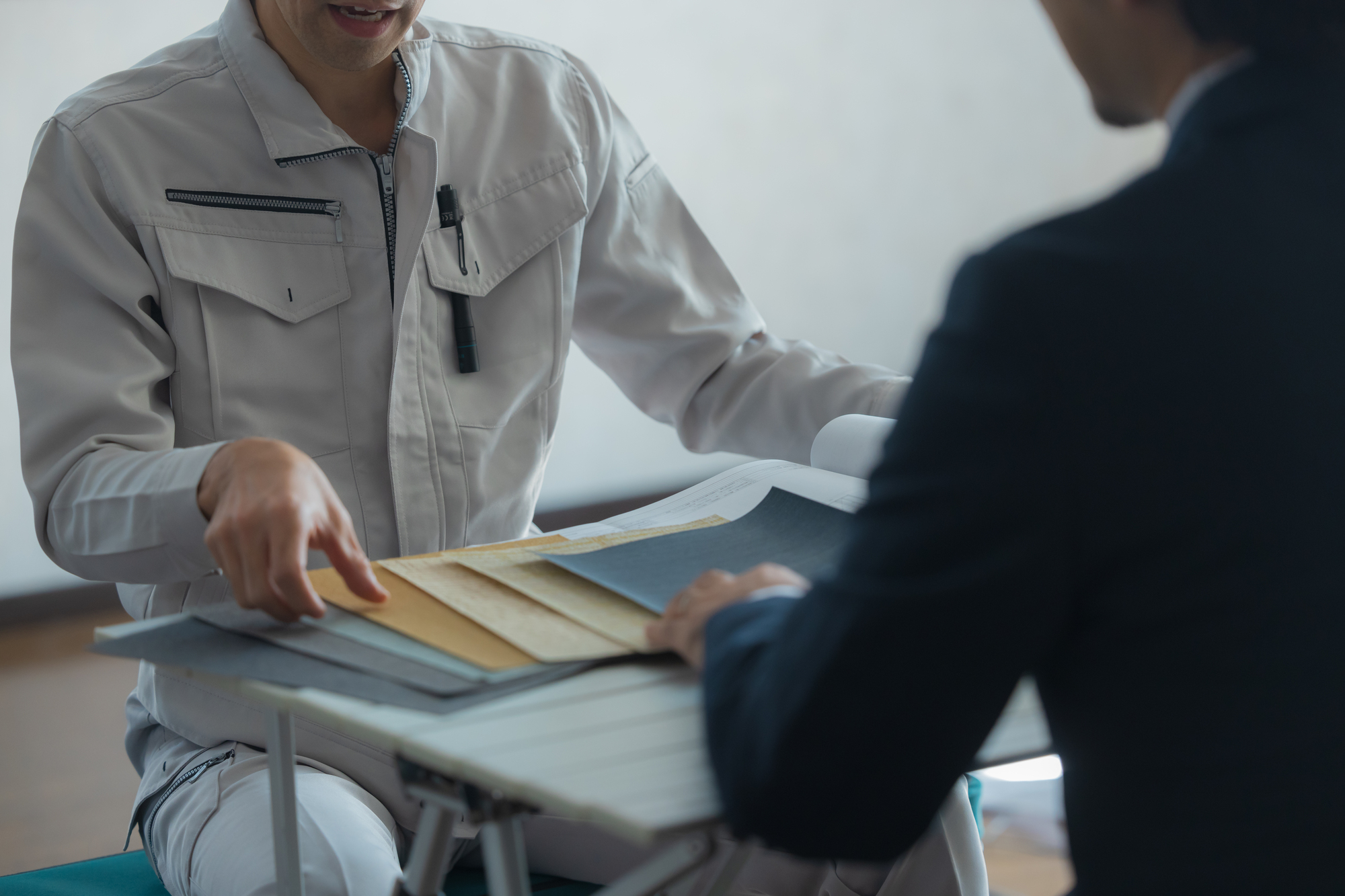 資料を手に打ち合わせをする作業着の男性とスーツの男性