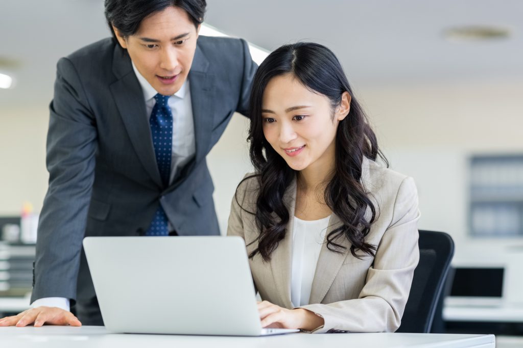 オフィスでパソコンを見ながら話す2人のビジネスパーソン