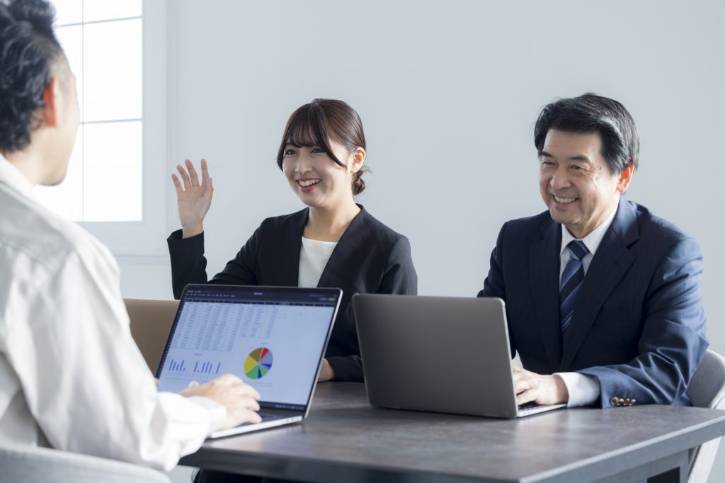 パソコンを置いたデスクに座り会議する3人のビジネスパーソン