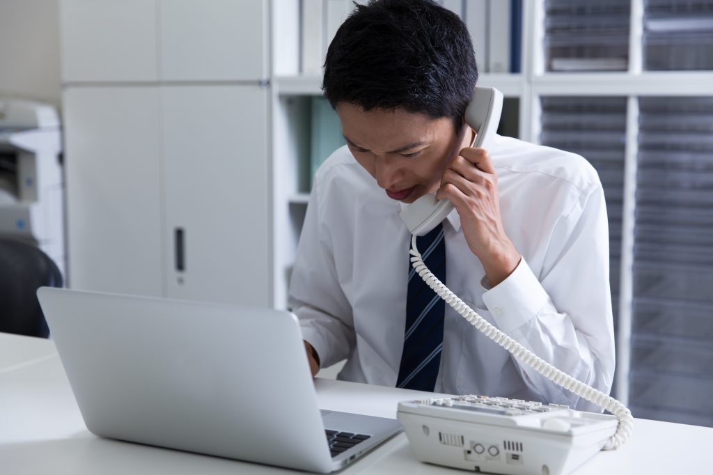 デスクでパソコンを前に電話するビジネスパーソン
