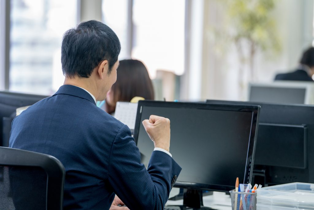 パソコンを見ながらガッツポーズをするビジネスパーソンの後ろ姿