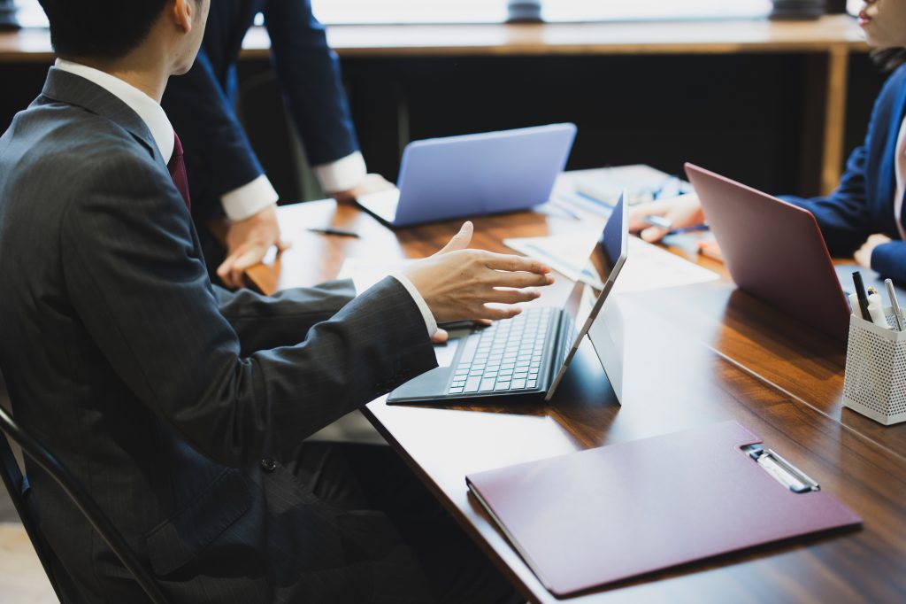デスクにパソコンや資料を置いて会議する3人のビジネスパーソン