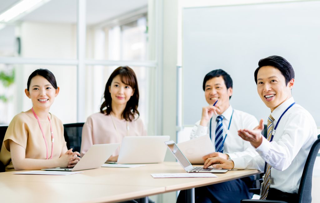 パソコンと資料を手に会議する4人のビジネスパーソン