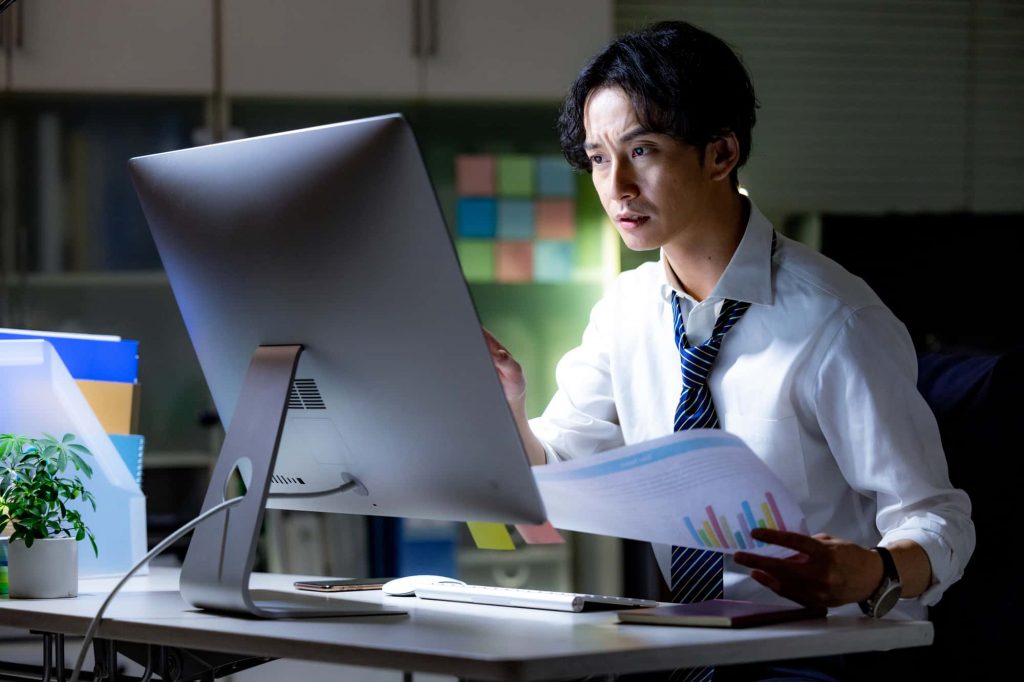 資料を手にパソコン作業をするビジネスパーソン