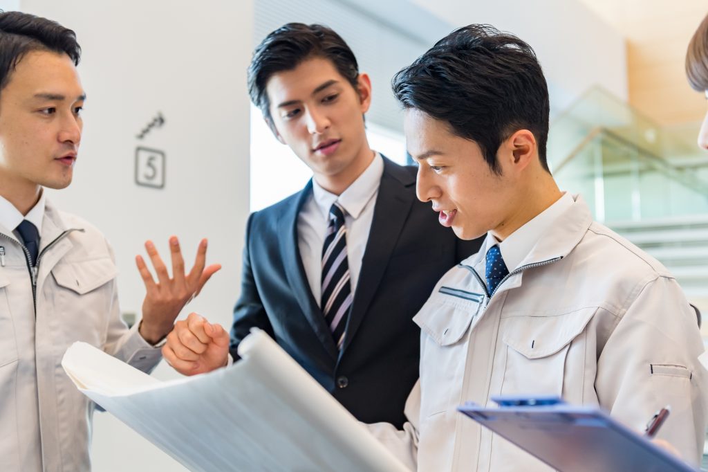 作業服を着た2人のビジネスパーソンとスーツを着たビジネスパーソンが打ち合わせする様子