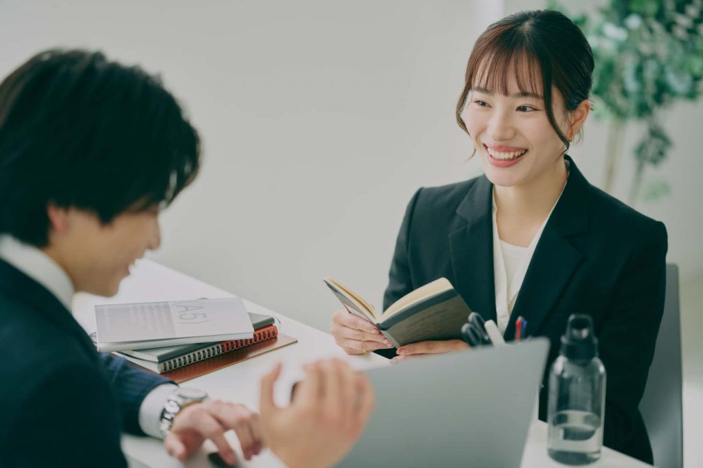 パソコンと手帳を見ながら打ち合わせをする2人のビジネスパーソン