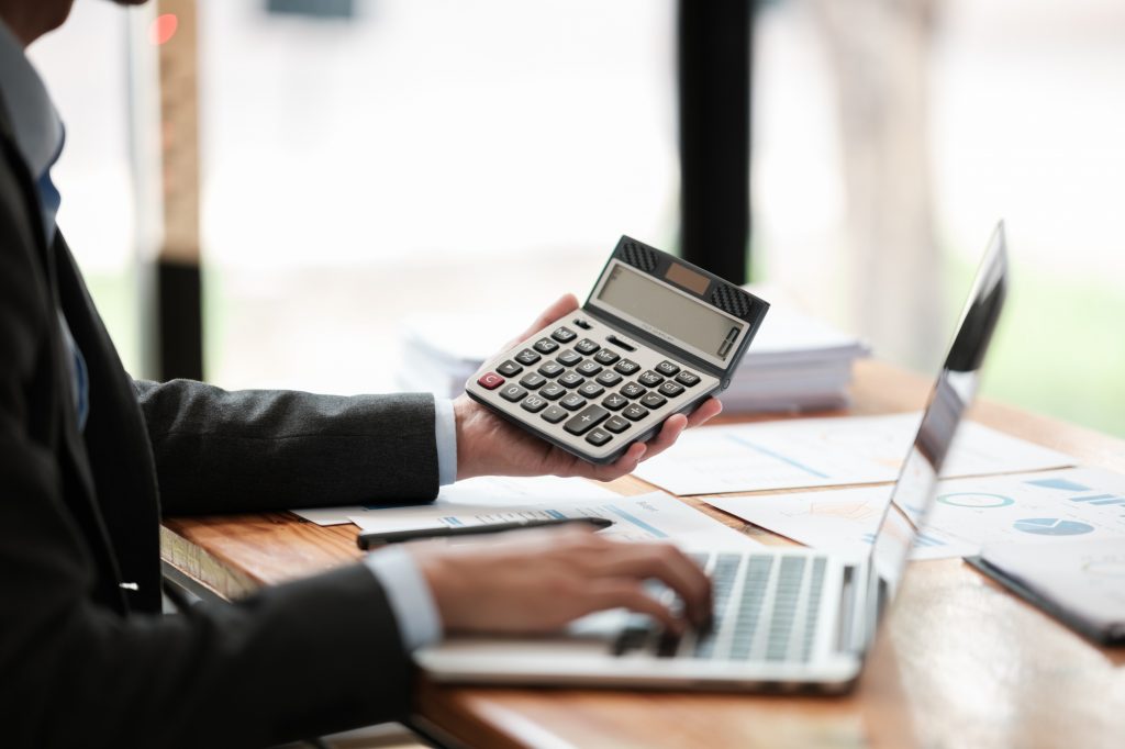 電卓を手にパソコン作業するビジネスパーソンの様子