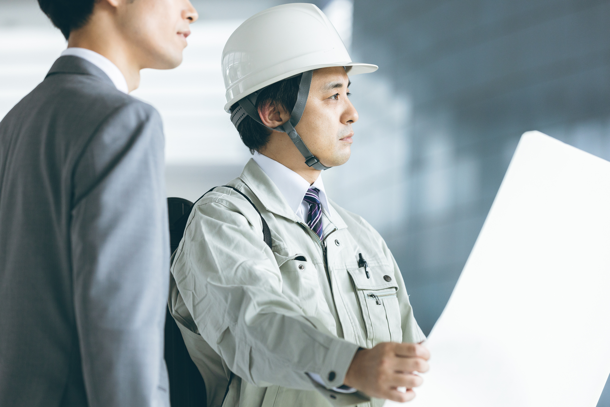 資料を見ながら打ち合わせする作業員とビジネスパーソン