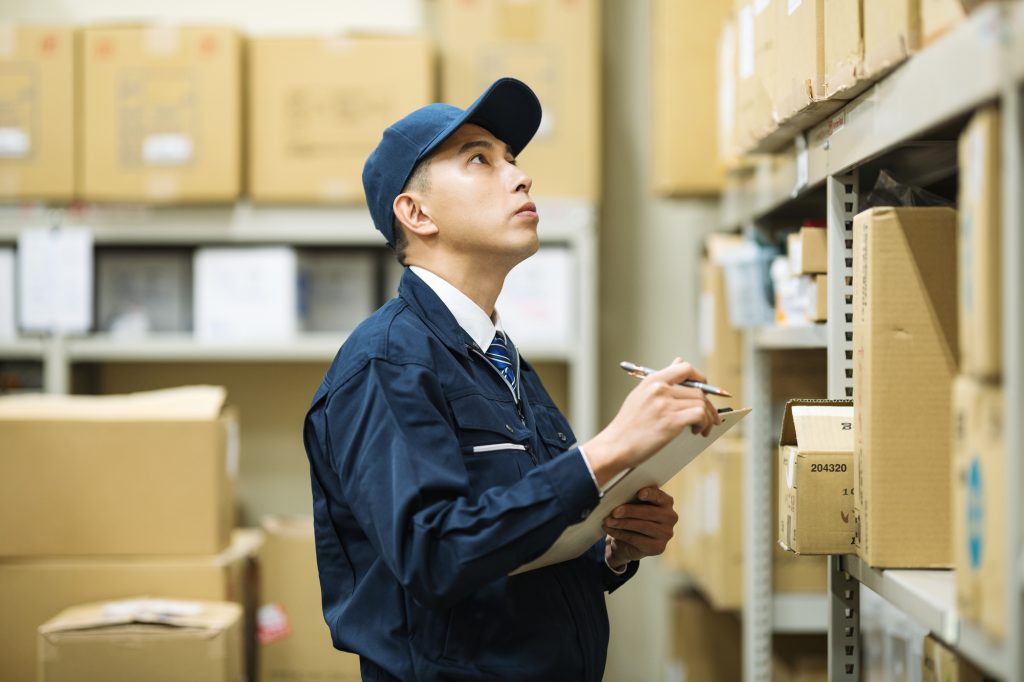 段ボールが積まれた倉庫で作業するビジネスパーソン