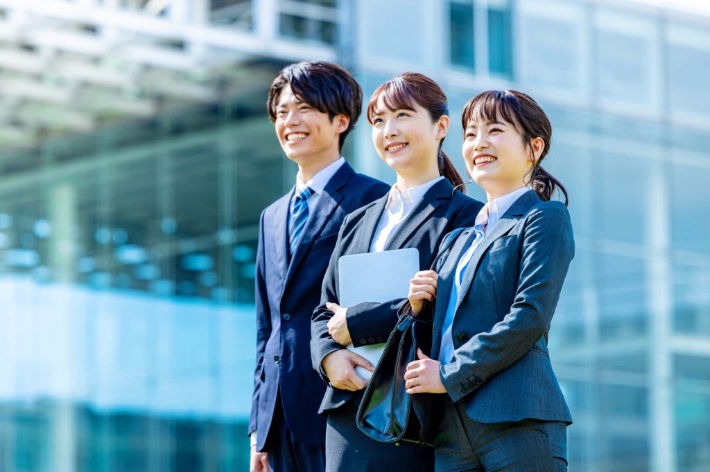 オフィスを背景にほほ笑む3人のビジネスパーソン
