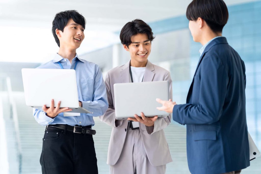 パソコンを持ちながら打ち合わせをする3人のビジネスパーソン