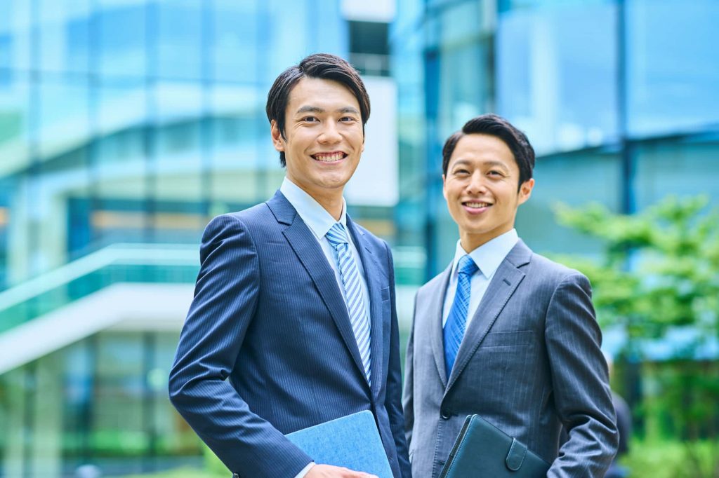 オフィスの前で笑顔で立つ2人のビジネスパーソン