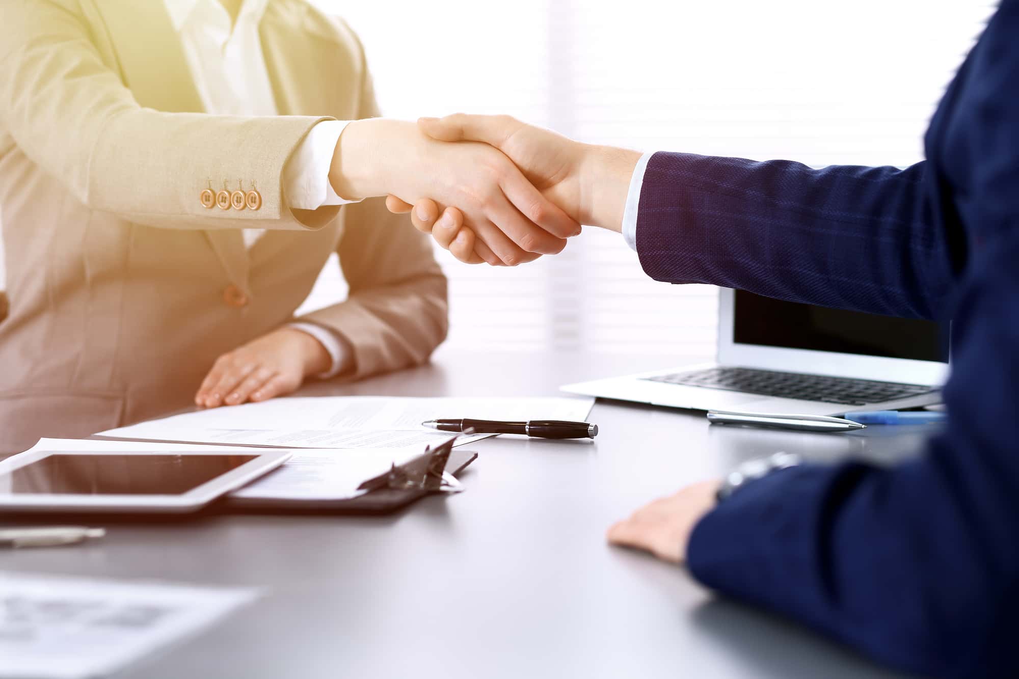資料が置かれたデスクの上で握手をする2人のビジネスパーソン