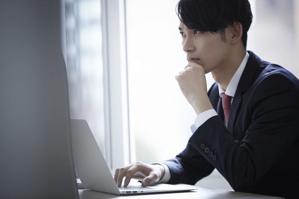 パソコン作業をしながら考え込むビジネスパーソン