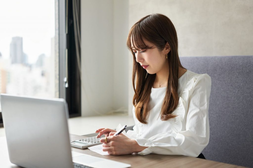 パソコンを開きながら電卓で作業するビジネスパーソン