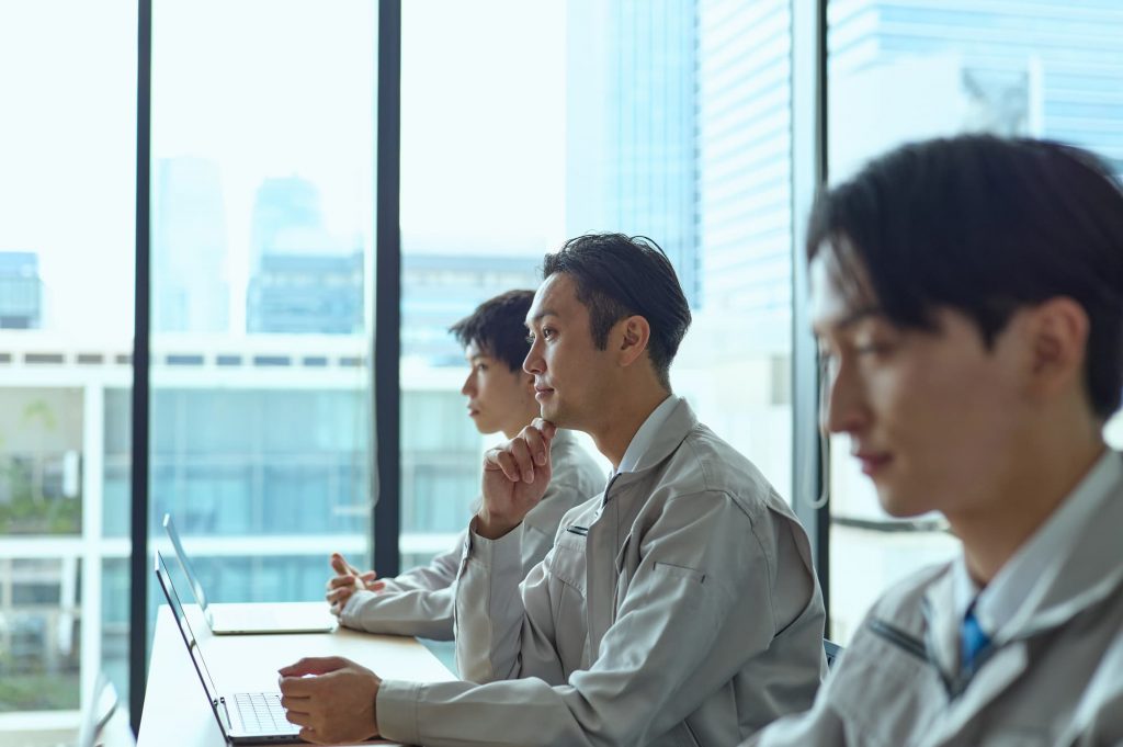 デスクに座る作業着を着た3人のビジネスパーソン

