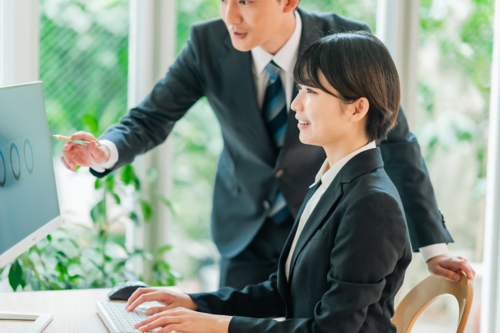 パソコン作業をしながら会話する2人のビジネスパーソン