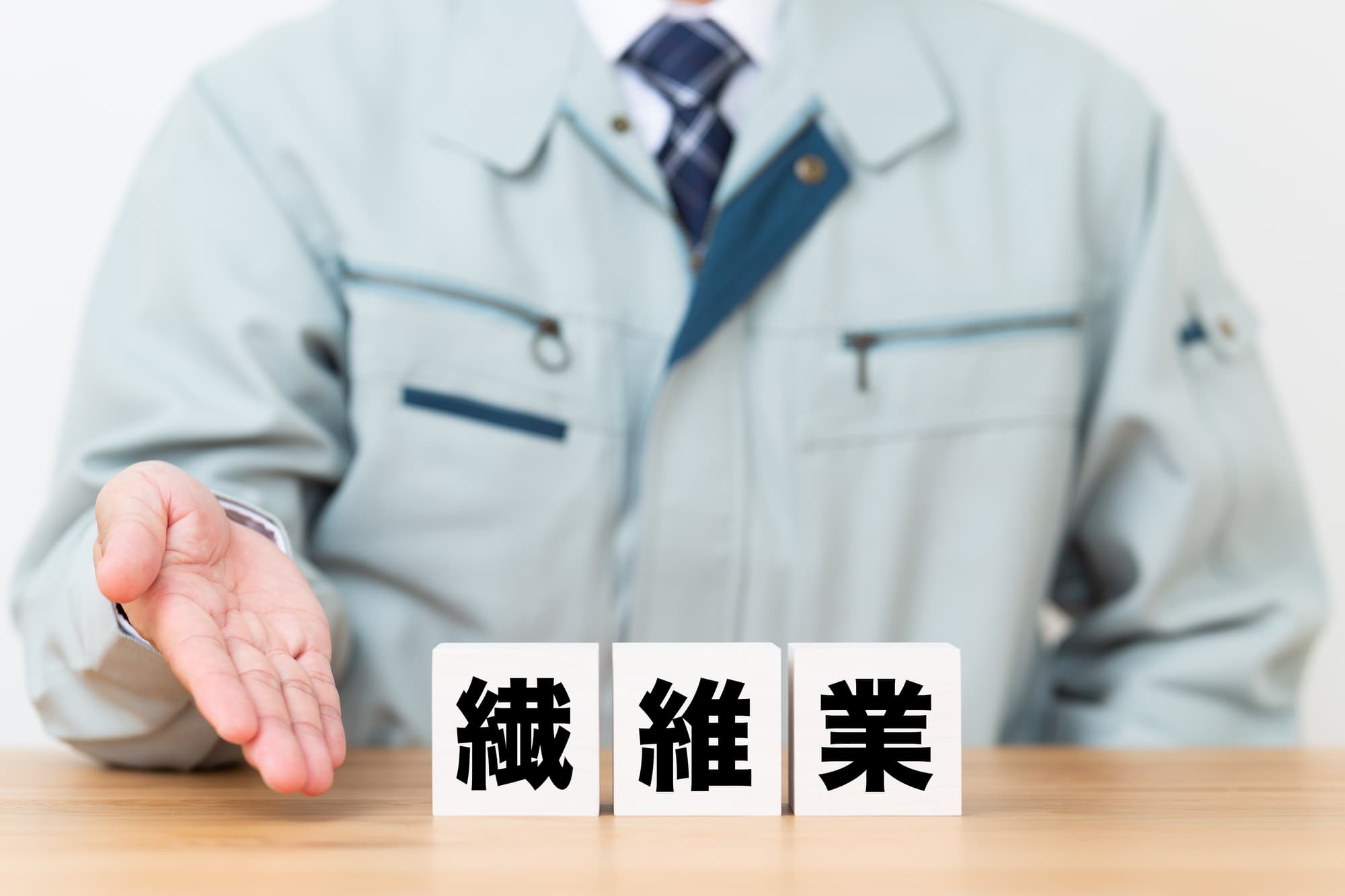 繊維業と書かれたブロックと作業着を着たビジネスパーソン