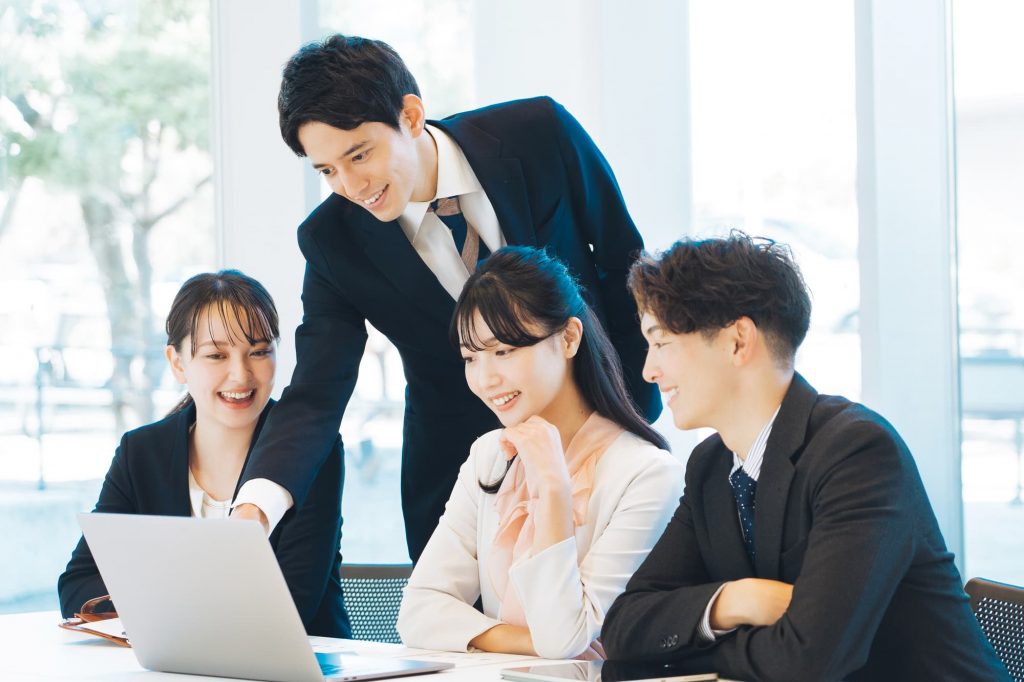 パソコンを見ながら笑顔で話をする4人のビジネスパーソン