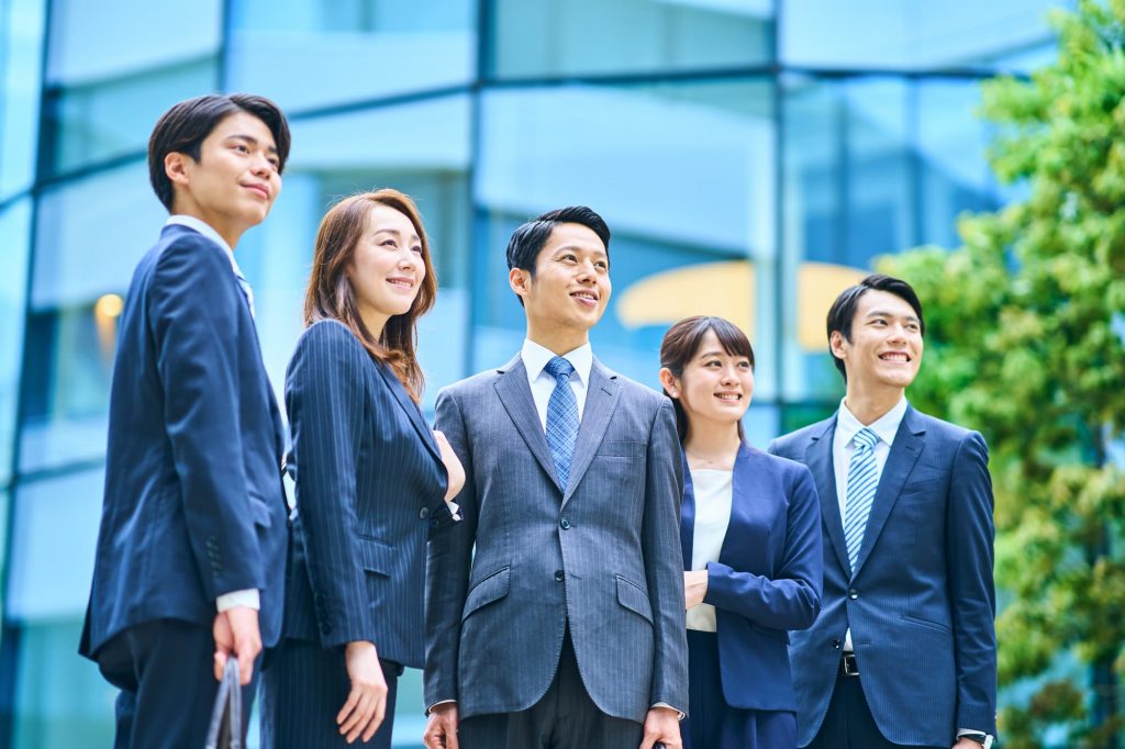オフィスの前で笑顔で立つ5人のビジネスパーソン