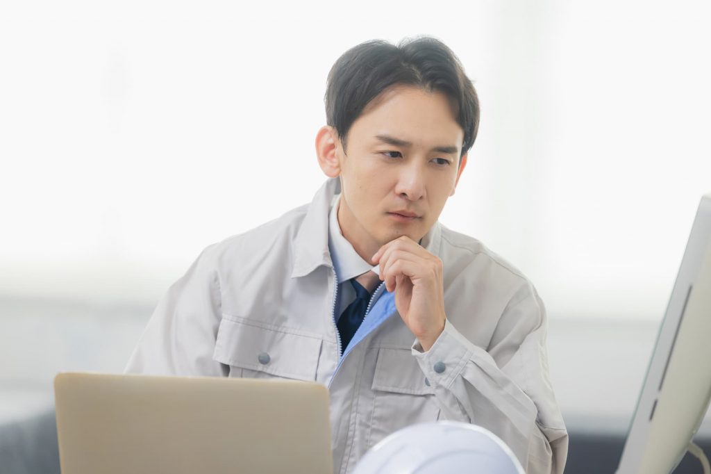 パソコンを見ながら悩む作業服を着たビジネスパーソン