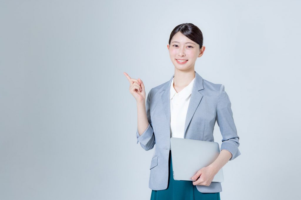 パソコンを持ちながら笑顔でひと差し指を立てるビジネスパーソン