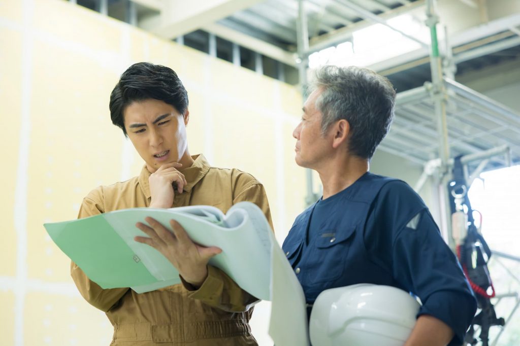 資料を見ながら悩む作業服の2人