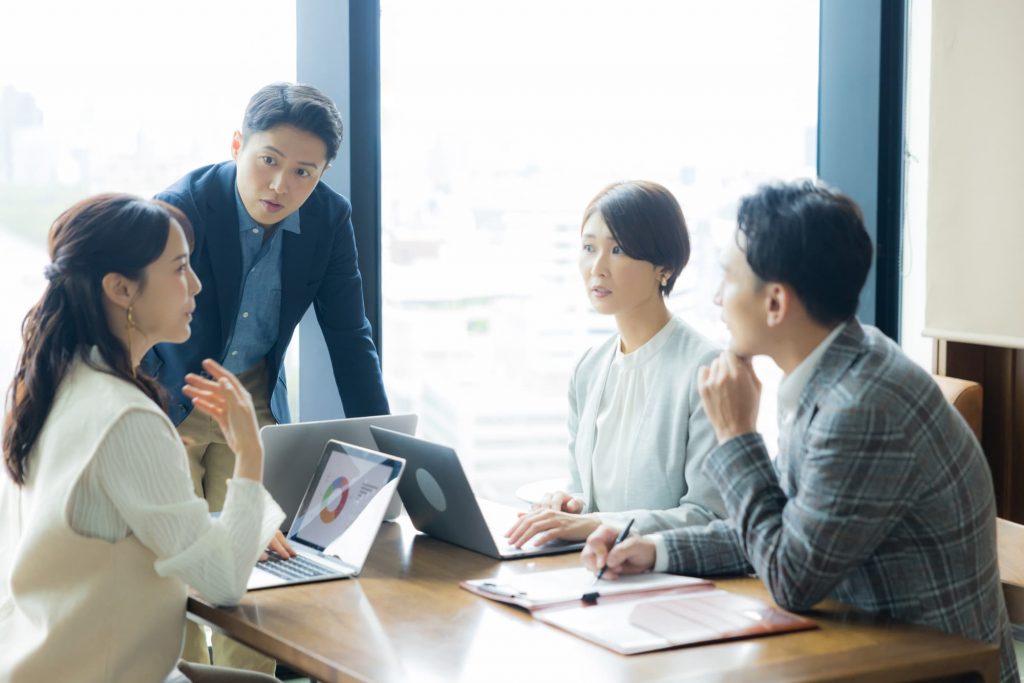 パソコンと資料が置かれたテーブルでミーティングする4人のビジネスパーソン